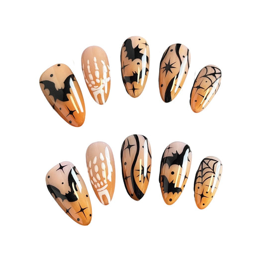 Haunted Nightfall press on nails, featuring hauntingly beautiful designs of bats, skeleton hands, spider webs, and cosmic stars over a soft nude-orange gradient