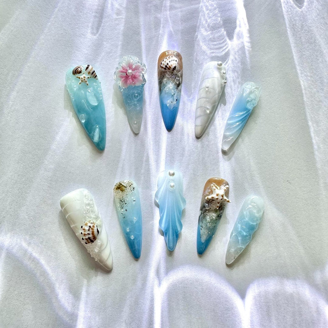 Handmade celestial press on nails featuring soft blues, whites, crescent shell, starfish, snails, and pearls.