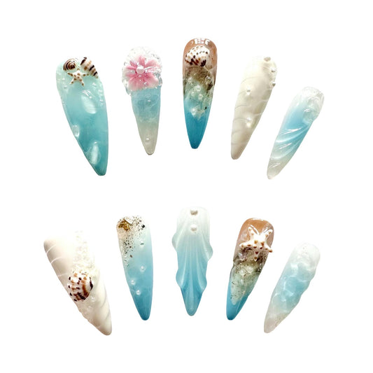 Handmade celestial press on nails featuring soft blues, whites, crescent shell, starfish, snails, and pearls.