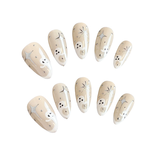 Star-Crossed Spirits Press On Nails, featuring cute ghostly figures and dazzling star-cross designs on a creamy nude base